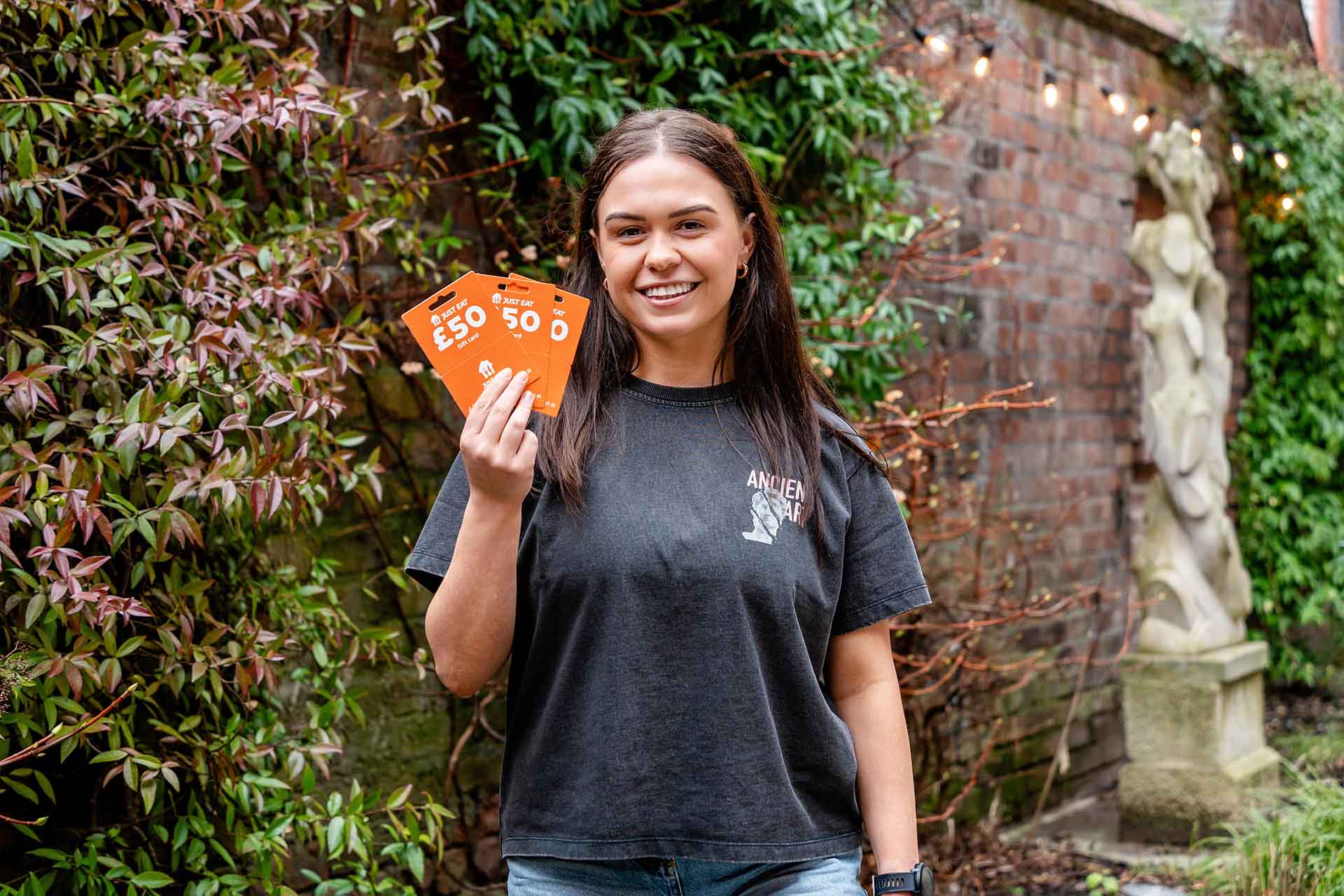 A headshot of student doctor Taia Rothwell holding three Just Eat vouchers. She has brown hair and is wearing a grey t shirt.