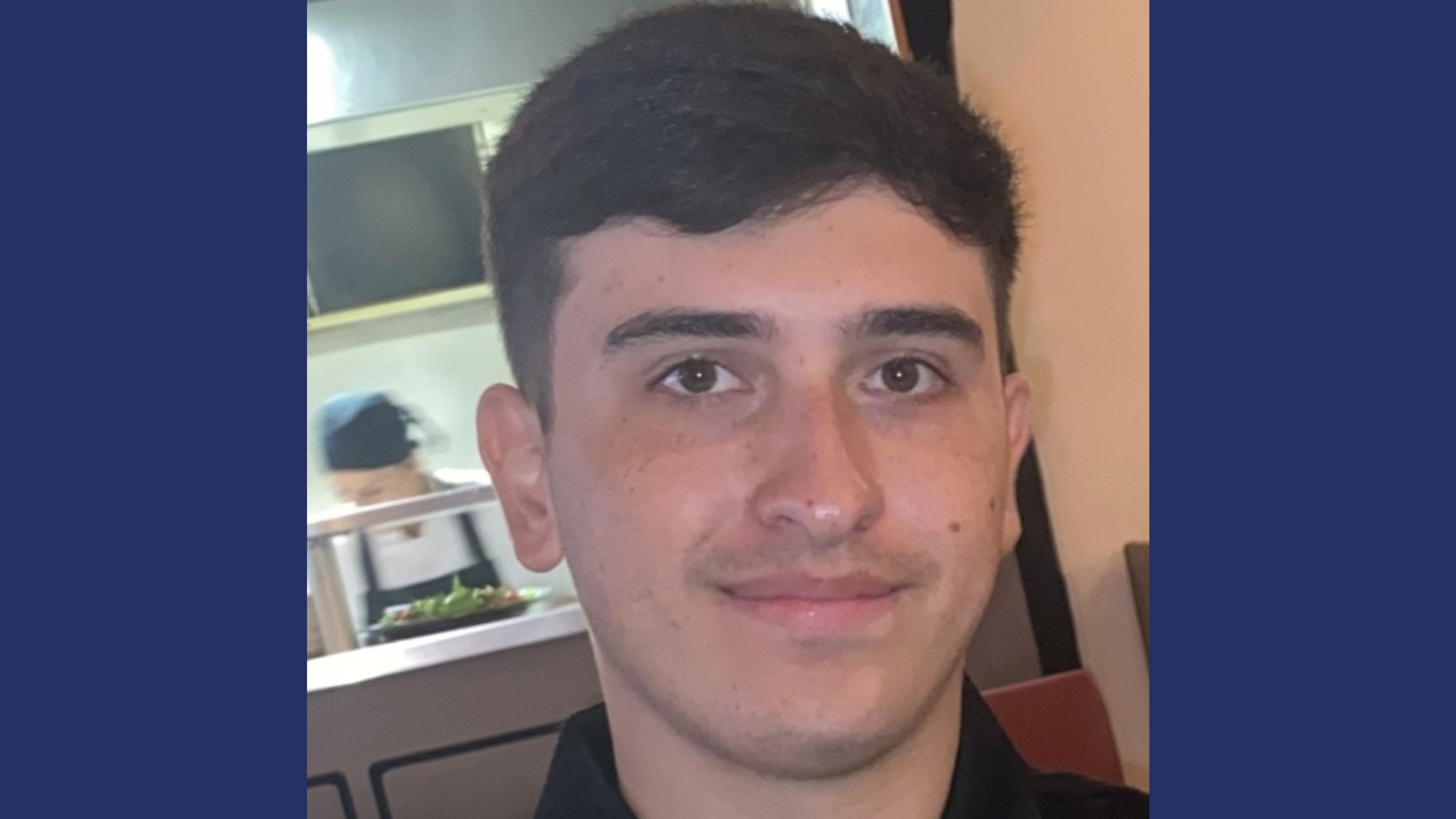 man with dark hair smiling to camera in restaurant