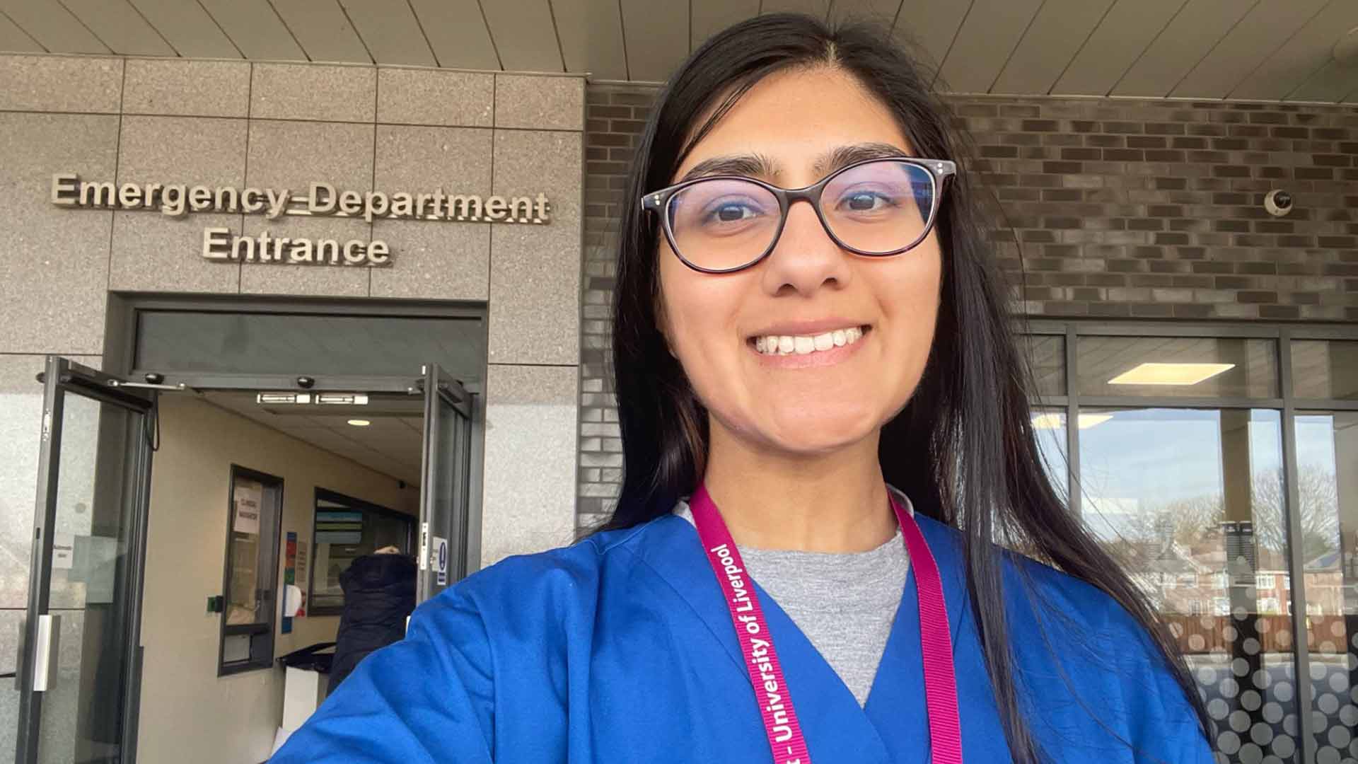 student doctor at A&E entrance wearing blue scrubs with ACE lanyard