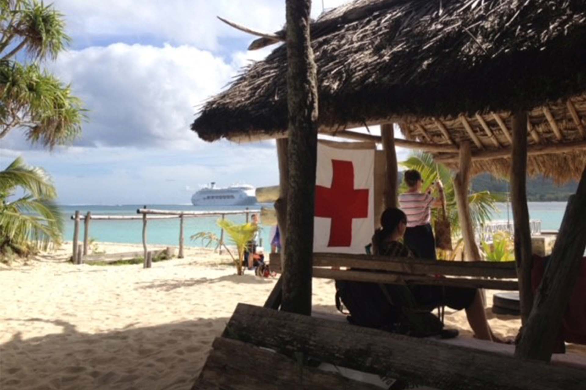 red cross flag on beach with cruise ship in background
