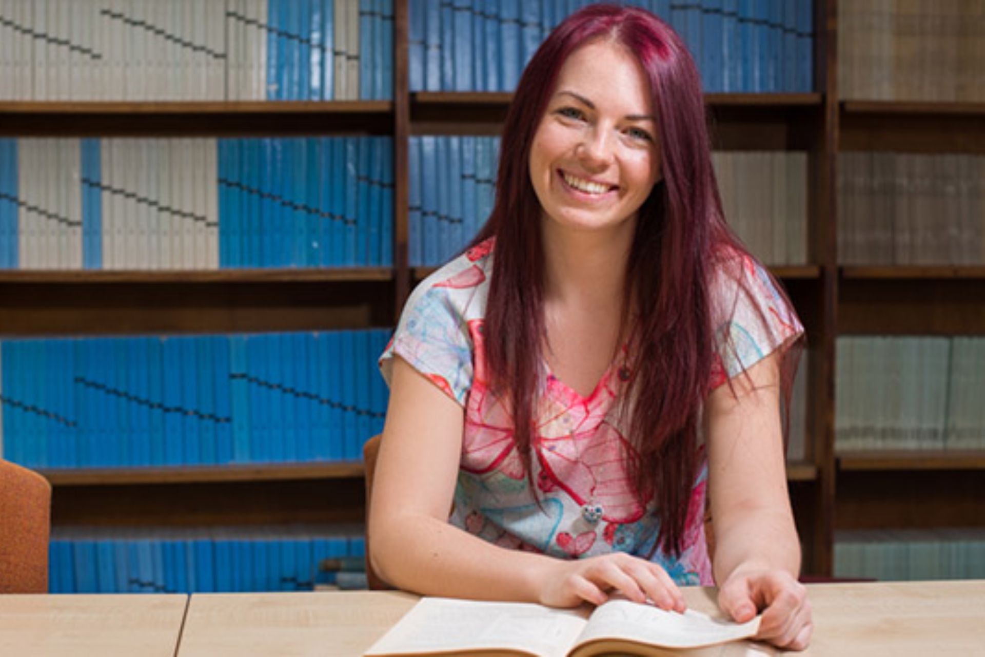 Postgraduate student sat in front of bookshelf