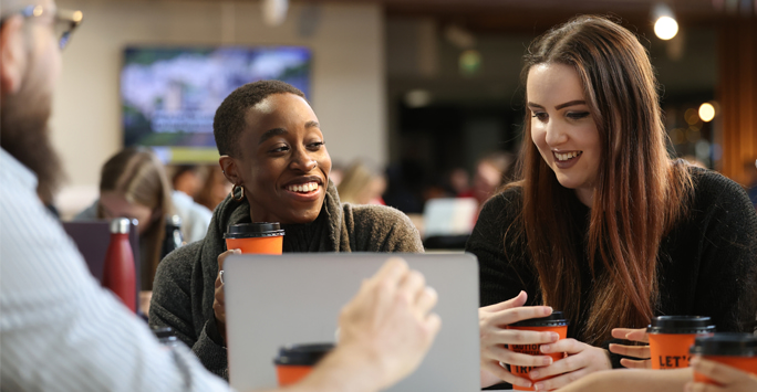 Students sit together at a table holding coffee cups.