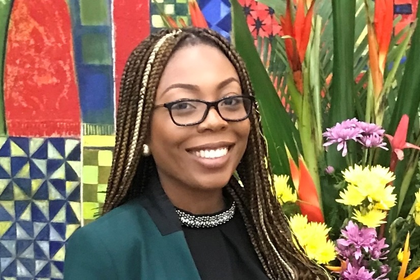 Victoria Williams, the West African Representative (Kaplan), looks to camera and smiles.