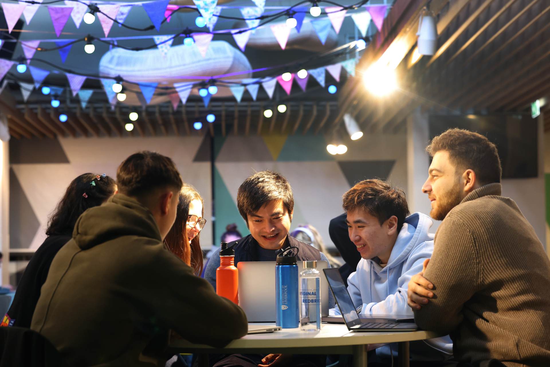 A group of students are sat around a table in the Guild of Students talking and laughing.