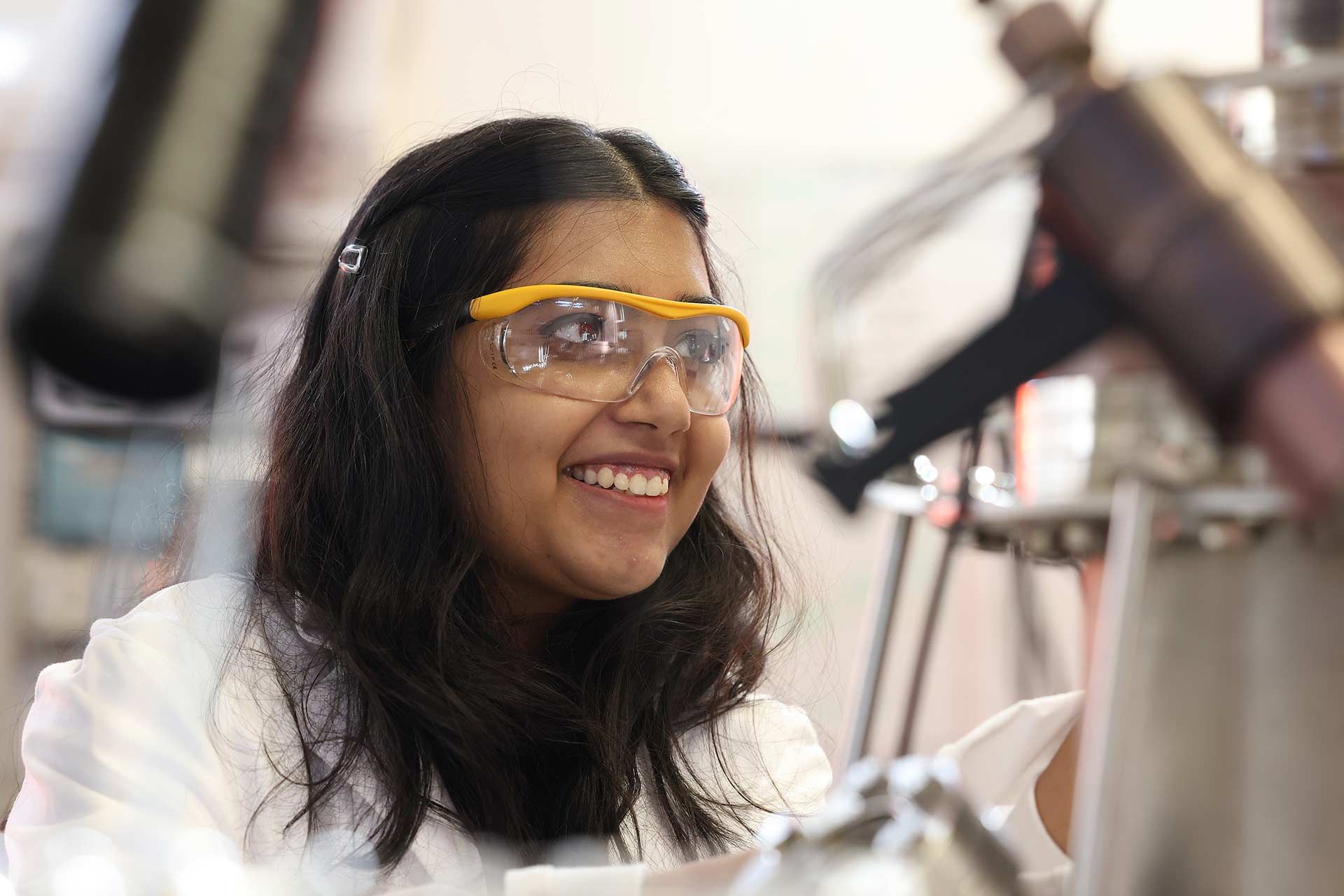 A student working in a laboratory, wearing a lab coat and protective goggles.