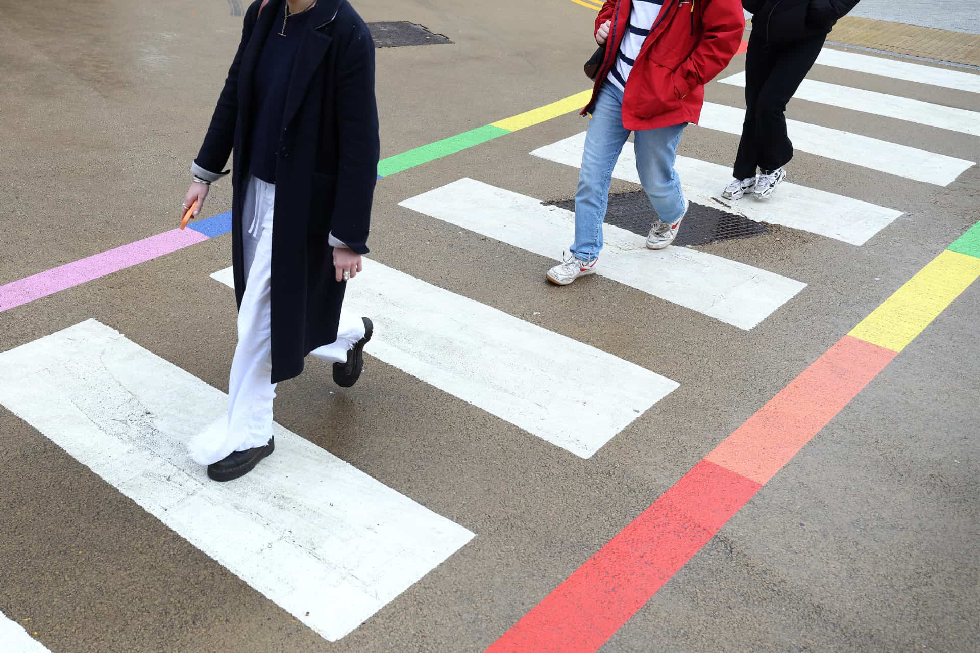 Three people walking across a crosswalk with rainbow colouring on the sides.