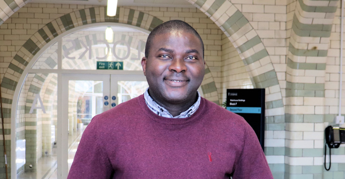 A photograph of Dr Adeniyi Olagunju standing in the corridor of a building at the University of Liverpool