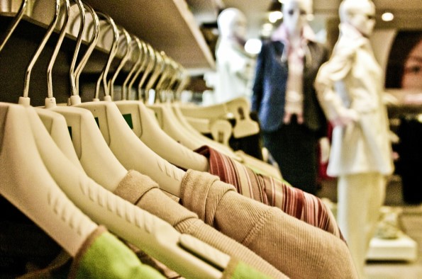 clothes hanging on a rail in a shop with mannequins in the background