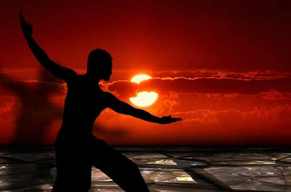 Man practicing Tai Chi silhouetted in front of a sunset