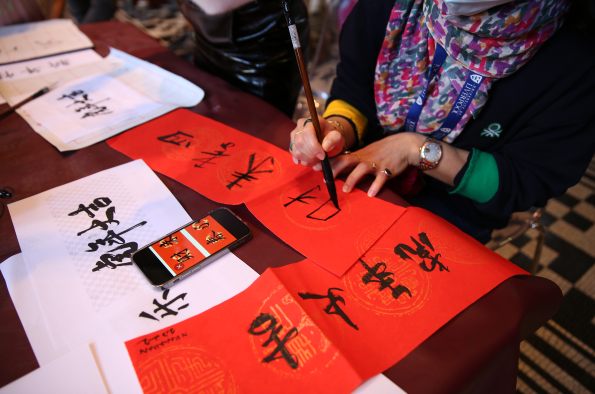 person visible from neck down writing Chinese calligraphy on red paper