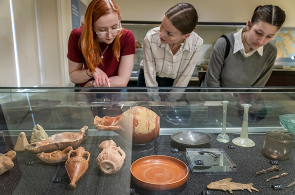 Three people look at ancient artifacts